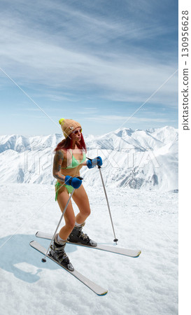 Female skier in bikini standing with poles on snowy mountain with confident smile. Hand made collage 130956628