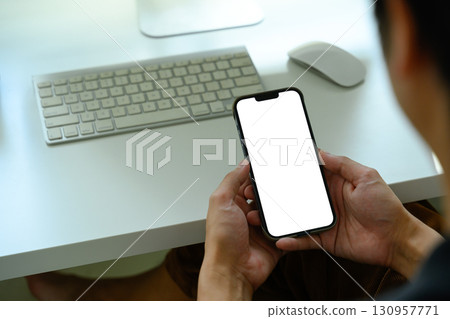 Close up of person holding smartphone with blank white screen at modern office desk Close up of person holding smartphone with blank white screen at modern office desk 130957771