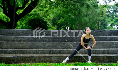 Young woman stretching legs outdoors on stone step in an open-air urban park environment 130957818