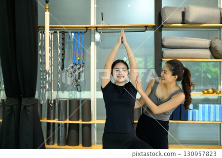 Smiling woman practicing yoga with personal trainer assistance during workout session Smiling woman practicing yoga with personal trainer assistance during workout session 130957823