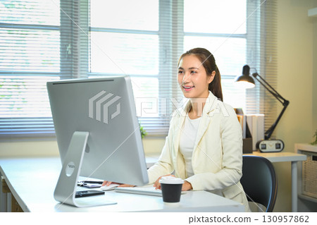 Confident female entrepreneur focused on online tasks in a bright office workspace. 130957862