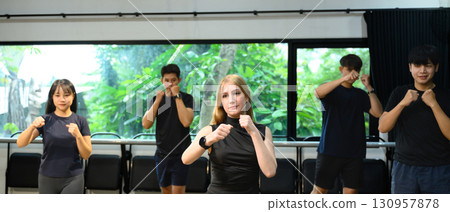 Group of young adults practicing boxing moves together in a bright indoor fitness studio 130957878