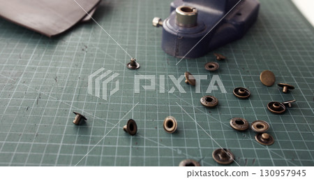 Leather pieces with metal rivets and press tool on green cutting mat Leather pieces with metal rivets and press tool on green cutting mat 130957945