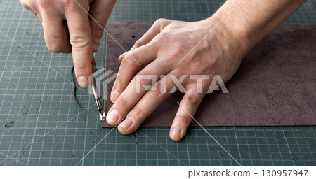 Craftsman using edge tool on leather strip for handmade leather goods production 130957947