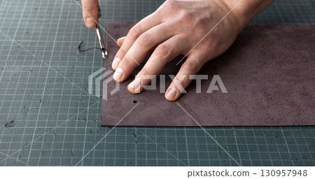 Craftsman using edge tool on leather strip for handmade leather goods production 130957948