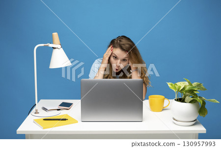 Shocked young woman looking at laptop screen while sitting at desk indoors 130957993