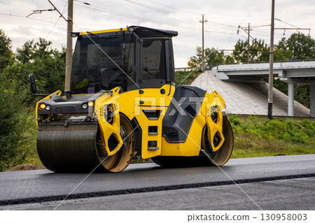 Modern yellow asphalt roller compacting new pavement at road construction project 130958003