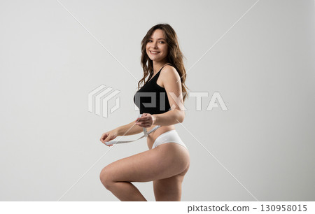 Smiling young woman measuring waist with tape in underwear for fitness and health 130958015