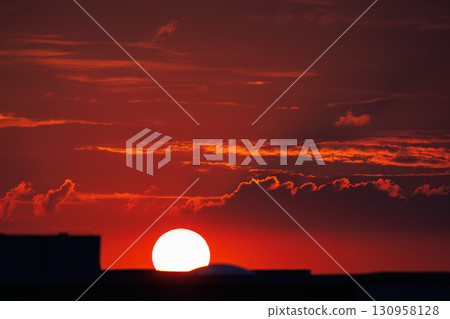 Stunning fiery sunset scene with vibrant red sky glowing sun setting behind city buildings urban silhouettes, creating warm dramatic atmosphere. Tranquil horizon dusk cloudscape Stunning fiery sunset scene with vibrant red sky glowing sun setting behind city buildings urban silhouettes, creating warm dramatic atmosphere. Tranquil horizon dusk cloudscape 130958128
