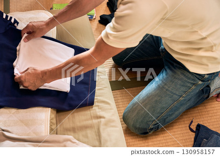 A series of photographs of a man sitting on a tatami mat and folding laundry. A man doing housework. A series of photographs of a man sitting on a tatami mat and folding laundry. A man doing housework. 130958157