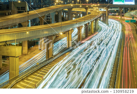 A nightscape view with bright glowing light trails effect of many cars headlights and rear lights on urban expressway. 130958219