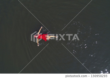 Aerial view of gorgeous woman in red dress floating on calm water Aerial view of gorgeous woman in red dress floating on calm water 130958293
