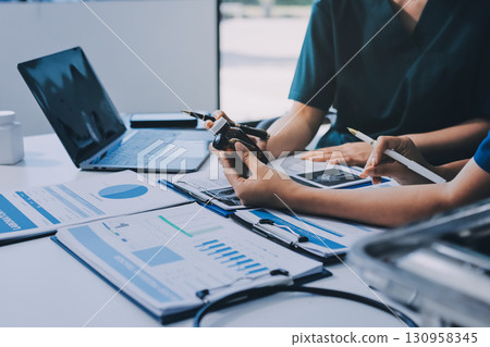 Two doctors and a female nurse meet at a table in the hospital, collaborating on medical tasks using laptops and computers 130958345