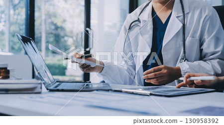 Medical team meeting analyzing blood test results in hospital laboratory. Doctors and scientists in lab coats are having a discussion about blood test result, holding test tubes and taking notes. 130958392