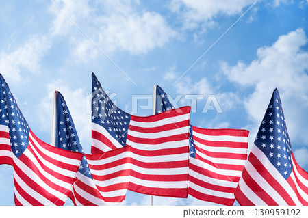 Waving United States flags on bright sky backdrop, symbol of liberty and democracy. Background for Memorial Day posters, Veterans Day banners, and patriotic holiday designs. 130959192
