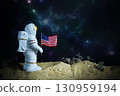 Small astronaut statue on alien desert landscape with USA flag, symbol of space travel, cosmic adventure and moon landing. Astronaut model in cosmic environment. 130959194