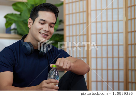 Healthy Lifestyle. Young man enjoying hydration with water bottle and headphones. Healthy Lifestyle. Young man enjoying hydration with water bottle and headphones. 130959356