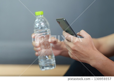 Modern Lifestyle. Young man holding a water bottle and smartphone, promoting wellness. Modern Lifestyle. Young man holding a water bottle and smartphone, promoting wellness. 130959357