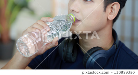 Wellness. Young man enjoying hydration while drinking water from a bottle. Wellness. Young man enjoying hydration while drinking water from a bottle. 130959380