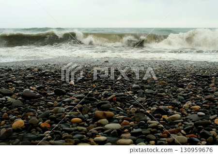 Stormy sea waves crushing on pebble beach with white foam in overcast weather. 130959676
