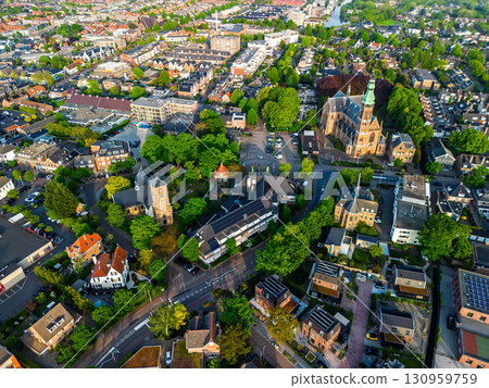 A European town with a tall green-spired church at its center, surrounded by houses, gardens, and winding streets, blending historic architecture with lush green spaces. A European town with a tall green-spired church at its center, surrounded by houses, gardens, and winding streets, blending historic architecture with lush green spaces. 130959759