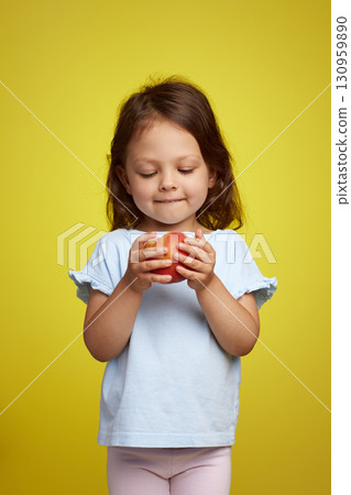 Portrait of brunette little child girl with peach on yellow background Portrait of brunette little child girl with peach on yellow background 130959890