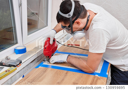 repairman using electric jigsaw and cutting hole for the sink in the kitchen countertops 130959895