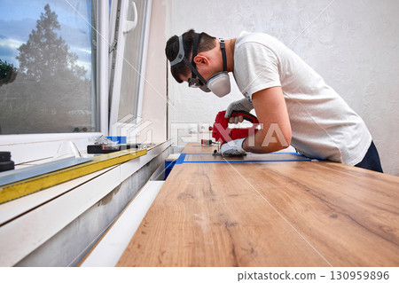 repairman with electric jigsaw doing sawing place for installing hob in a worktop in the kitchen repairman with electric jigsaw doing sawing place for installing hob in a worktop in the kitchen 130959896