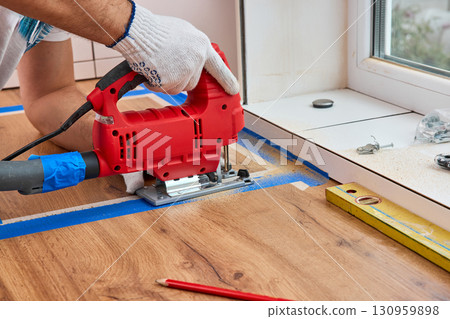 repairman using electric jigsaw and cutting hole for the sink in the kitchen countertops 130959898