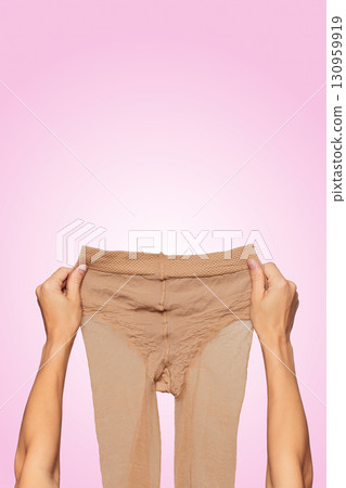 female hands holding beige nylon pantyhose on pink background. female hands holding beige nylon pantyhose on pink background. 130959919