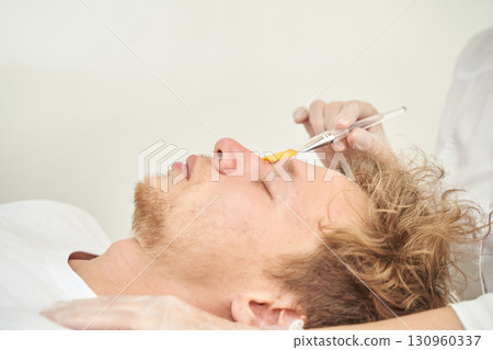 Caucasian male receiving facial treatment with brush by professional in spa Caucasian male receiving facial treatment with brush by professional in spa 130960337