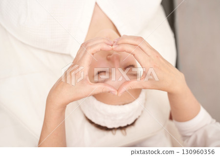 Relaxed young caucasian female making heart shape with hands during spa facial 130960356