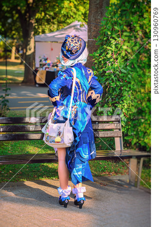 Person in an elaborate blue fantasy cosplay costume stands by a park bench with decorated bag. Concept of cosplay, creativity, anime fantasy character fashion 130960769