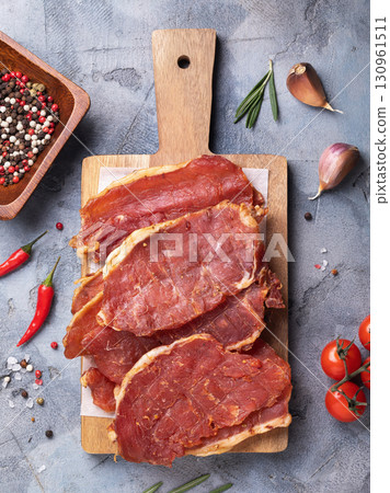 Top view of pieces of smoked pork on wooden tray surrounded by various ingredients on table Top view of pieces of smoked pork on wooden tray surrounded by various ingredients on table 130961511