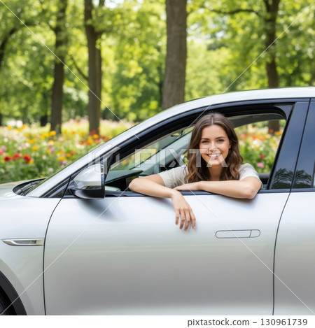 Young Woman Enjoying a Sunny Day by a Modern Car in Garden Setting 130961739