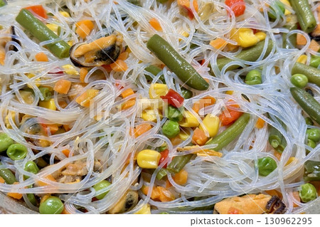 This bright and colorful dish consisting of rice noodles, fresh vegetables and juicy mussels in a pan in a home kitchen is ideal for healthy eating. Close-up. This bright and colorful dish consisting of rice noodles, fresh vegetables and juicy mussels in a pan in a home kitchen is ideal for healthy eating. Close-up. 130962295