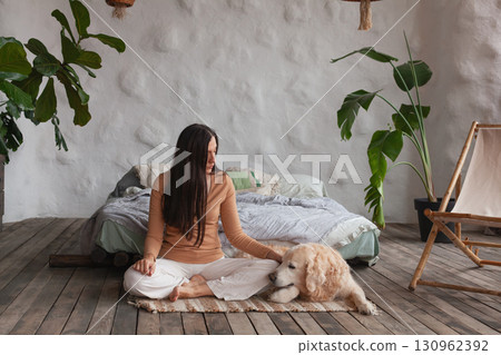 Mindful woman practicing yoga with her golden retriever in a cozy hotel room 130962392