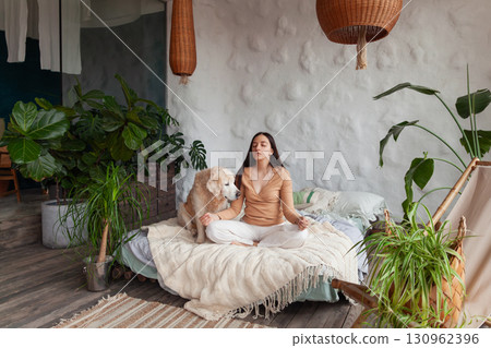 Mindful woman practices yoga with her friendly golden retriever in a cozy hotel room Mindful woman practices yoga with her friendly golden retriever in a cozy hotel room 130962396
