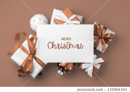 Merry christmas background, paper holiday greeting card on gift boxes and xmas ball on mocha mousse color background Merry christmas background, paper holiday greeting card on gift boxes and xmas ball on mocha mousse color background 130964304