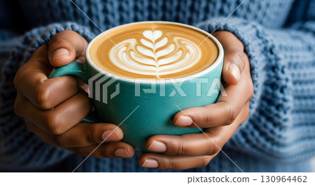 Hands holding a teal coffee mug with beautiful latte art, representing comfort and relaxation. 130964462