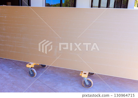 Large construction drywall on wheeled cart inside building under renovation 130964715