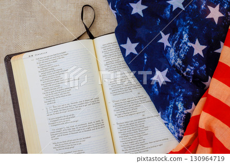 Bible opened next to patriotic American flag, symbolizing faith national pride during quiet reading session 130964719