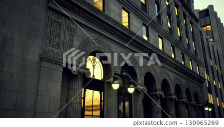 Beautifully detailed historic building showcases intricate stonework and arched windows, illuminated by a warm sunset glow reflecting off its façade. 130965269