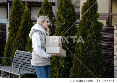 Woman carrying cardboard boxes while walking in residential area 130965373