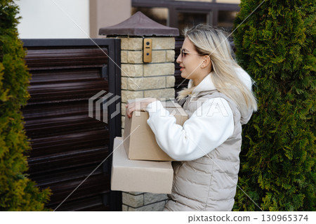 Delivery woman carrying packages in front of a house gate Delivery woman carrying packages in front of a house gate 130965374
