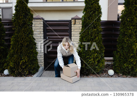 Woman picking up delivered cardboard boxes in front of her house 130965378