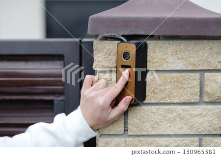 Woman pressing button on modern video intercom system at building entrance Woman pressing button on modern video intercom system at building entrance 130965381