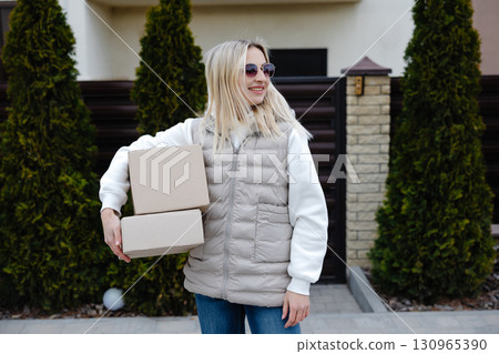 Delivery woman carrying cardboard boxes in front of a house Delivery woman carrying cardboard boxes in front of a house 130965390