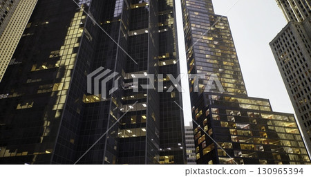 Tall, dark skyscrapers rise against a gray sky, with illuminated windows showcasing urban activity. This cityscape captures the energy and vibrancy of metropolitan living. Tall, dark skyscrapers rise against a gray sky, with illuminated windows showcasing urban activity. This cityscape captures the energy and vibrancy of metropolitan living. 130965394