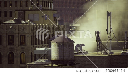 Morning light highlights an urban skyline featuring a classic water tower. Steam rises from buildings, creating an atmospheric city view filled with character and activity. 130965414